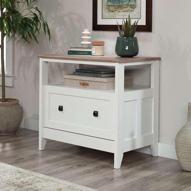 Sauder August Hill lateral file in soft white finish with wood grain top, featuring one drawer with black handles and an open shelf holding books and a storage box.