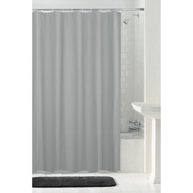 Hometrends Waterproof Herringbone Fabric Shower Curtain Liner in grey with metal grommets and weighted magnetic hem, hanging on a shower rod in a white tiled bathroom with a bathtub, chrome showerhead, and dark grey bath mat, suitable for use alone or paired with a decorative curtain.