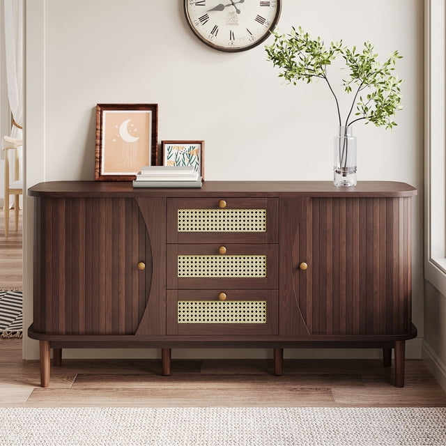 MODERNLUXE Rattan Sideboard Buffet Cabinet with Storage in walnut finish, featuring three rattan drawers, sliding doors, and adjustable shelves. The cabinet has rounded edges for safety and a stylish look, with solid wood legs and handles for durability. Measuring 55.3 inches in length, 15.8 inches in depth, and 29.9 inches in height, it is ideal for kitchens, living rooms, or hallways. The image shows the sideboard in a bright, modern room with decorative items on top, including framed art and a vase with greenery.