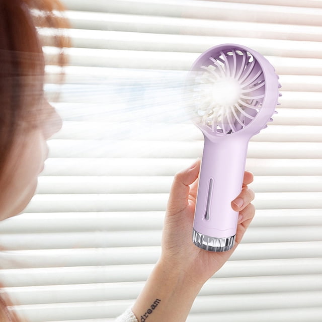TNDBKQWR Fan for Men Electric Portable Fan, a handheld USB rechargeable fan with a compact lavender design. This foldable mini fan features a built-in atomization function for cooling mist, ideal for travel, office, camping, and outdoor use. A person holds the fan near their face, with visible airflow and mist.