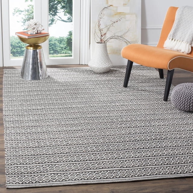 Safavieh Montauk Randall Tapis à Rayures Géométriques Comprenant du Coton Tissé à Plat avec des Rayures Géométriques Noires et Blanches sur un Plancher de Bois Franc, Style avec une Chaise orange, un vase Texturé Blanc avec des branches Séchées, une table d'Appoint Métallique avec des Livres et du Corail, et un pouf Tricoté Gris, Convient aux Intérieurs Côtiers à Contemporains.