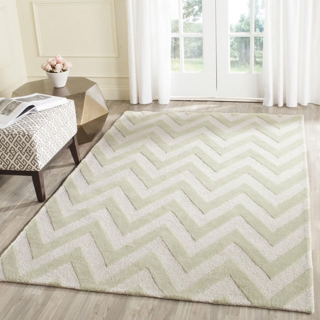 Safavieh Cambridge Kaitlyn Zig Zag Stripes Area Rug with hand-tufted wool construction, featuring plush cut and high/low loop piles in light green and cream zig zag stripes, displayed on a light wood floor in a bright room with white curtains and modern furniture, ideal for adding texture and classic American style to home or office spaces.