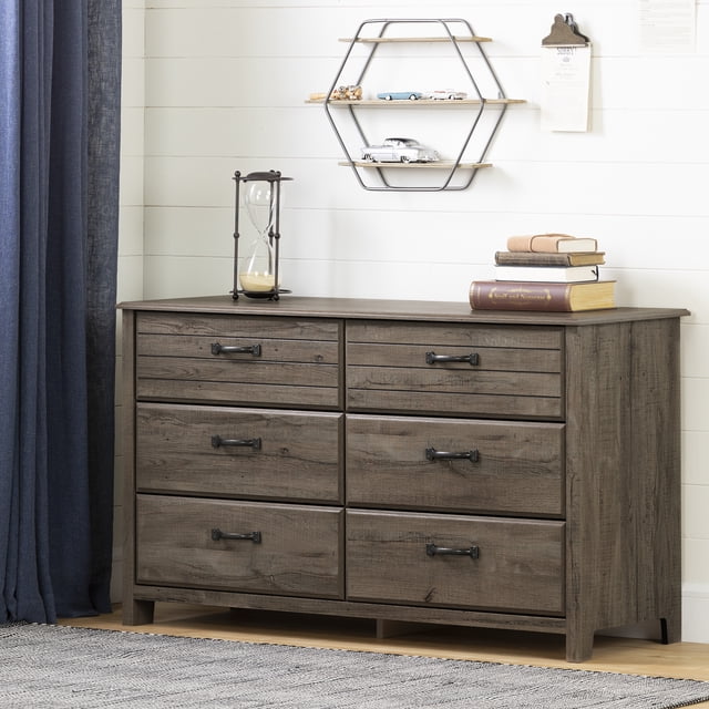 South Shore Ulysses 6-Drawer Dresser for Child in fall oak finish with six spacious drawers featuring metal handles and smooth metal slides, set against a white shiplap wall with a hexagonal wooden shelf holding toy cars, an hourglass and stacked books on top, placed on a light hardwood floor with a gray rug and navy curtains nearby.