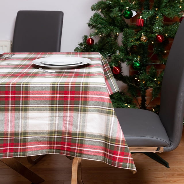 Celebration Plaid Table Cloth with a seamless red, green, and white checkered pattern covering a wooden dining table set with white plates and silverware, accompanied by gray leather chairs and a decorated Christmas tree, suitable for holiday dining and festive entertaining.
