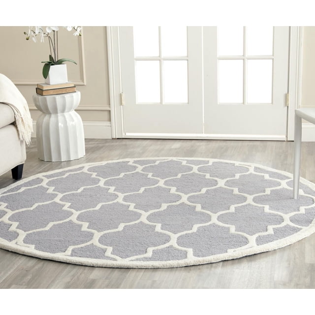 Safavieh Cambridge Kevin Geometric Area Rug, round hand-tufted wool rug with a light grey background and white geometric trellis pattern, displayed on light hardwood flooring in a bright room with white French doors, ideal for adding modern American style to home or office spaces.