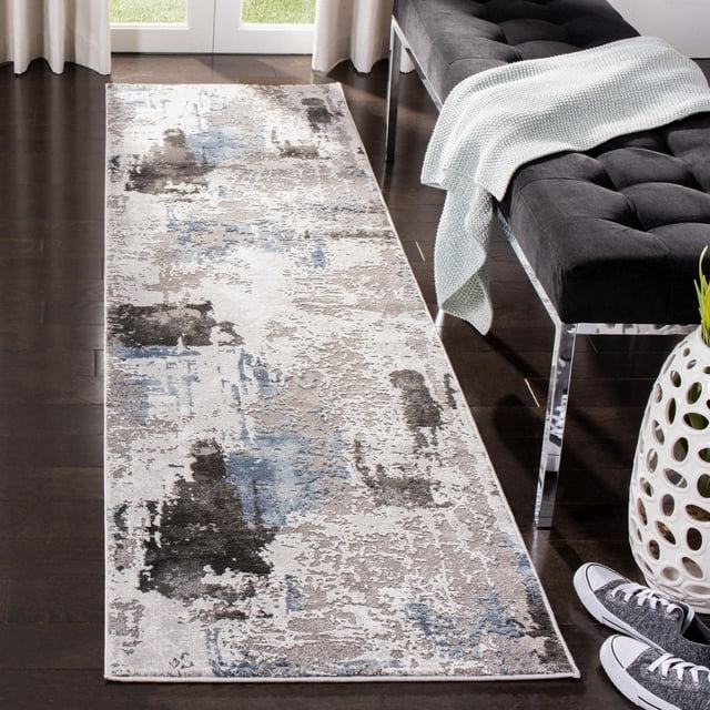 SAFAVIEH Craft Constantine Abstract Area Rug runner with swirling abstract patterns in muted blue, grey, and beige tones on a dark hardwood floor beside a black tufted bench with a light blue knitted throw and a white ceramic vase with cutout details, suitable for enhancing contemporary home interiors.