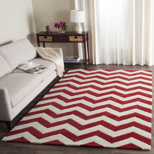 Safavieh Chatham Jake Zigzag Stripes Area Rug featuring hand-tufted wool with medium pile height, displaying bold red and cream zigzag stripes on a dark hardwood floor, styled in a living room with a beige sofa and dark wood console table, ideal for adding softness and contemporary flair to home interiors.