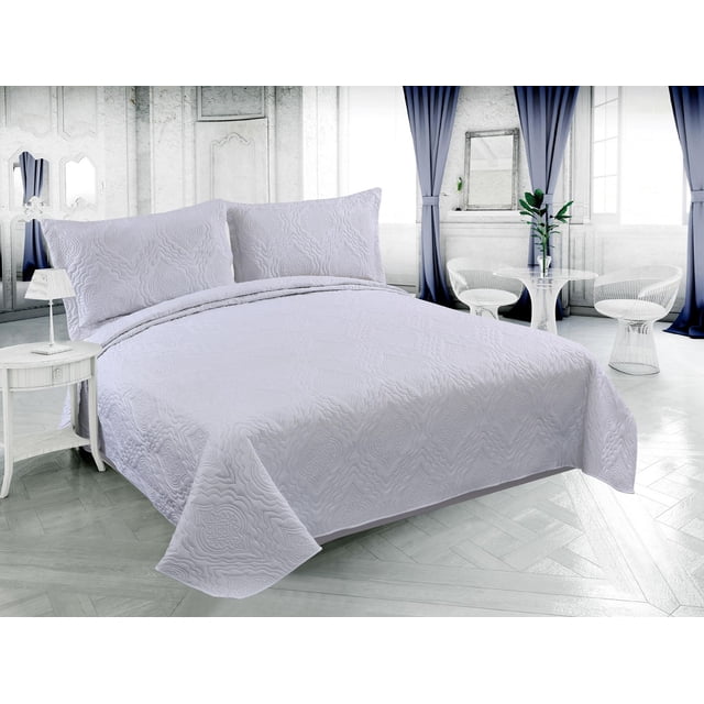 Marina Decoration Solid Embossed Pinsonic Coverlet Bedspread Bedding Ultra Soft Summer Quilt Set with Shams in white, featuring a subtle embossed floral pattern and two matching pillow shams on a bed in a bright room with grey parquet flooring, blue curtains, and white modern furniture. This lightweight, breathable quilt is suitable for summer use and often used as a versatile layering piece year-round.