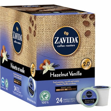 Zavida Single Serve Coffee Hazelnut Vanilla, 96 Cups. The image shows a box of Zavida Hazelnut Vanilla coffee pods, featuring a burlap texture design with coffee beans and vanilla flowers. The box contains 24 single-serve coffee cups, with medium roast flavor, compatible with Keurig 2.0 brewing systems. Proudly roasted in Canada, the coffee is 100% Rainforest Alliance certified, carbon neutral, and Kosher certified. A single pod is displayed next to the box.