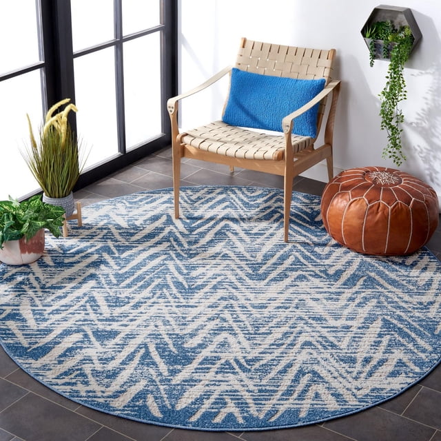 SAFAVIEH Cottage Tapis d'Intérieur/extérieur à Chevrons Ronni, Rond avec Motif à Chevrons Bleu et beige, Fibres Synthétiques Tissées Mécaniquement pour la Durabilité, Placé sur un Plancher de Tuiles Foncées avec une Chaise à Sangle Tressée en Bois avec Coussin Bleu, pouf en Cuir Brun et Plantes Vertes Près de Grandes Fenêtres dans une Pièce Lumineuse, Idéal pour les Zones Intérieures Ou Extérieures à Fort Passage.