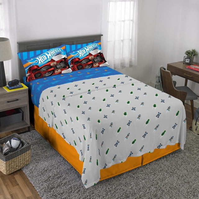 Hot Wheels "Fast Pace" full sheet set on a full-size bed with a blue fitted sheet featuring the Hot Wheels logo and a red race car, a grey flat sheet with small race car patterns, and reversible pillowcases showing colorful race cars, made of 100% polyester microfiber suitable for kids' bedrooms.