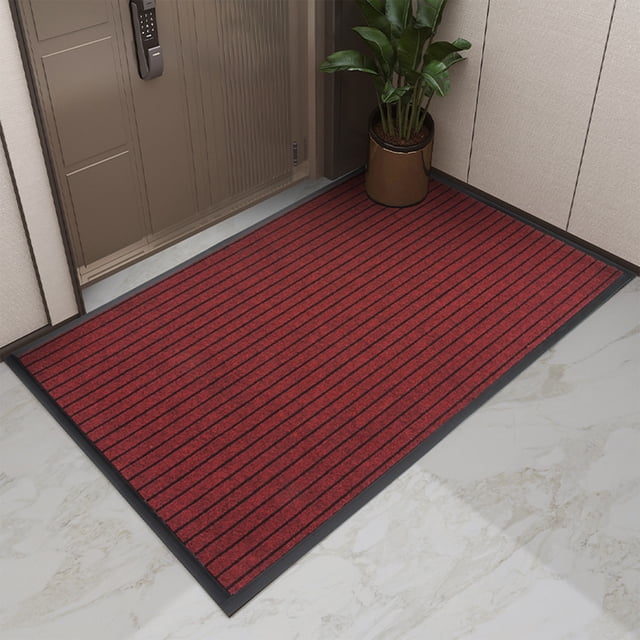 HOARBOEG Front Door Mat Welcome Mats, a red indoor and outdoor rug with black striped design, measuring 35.4 inches by 23.6 inches. Made of durable PVC and polyester with a non-slip backing, ideal for high-traffic areas like entryways, kitchens, and patios. Shown placed in a modern entryway with a potted plant nearby.