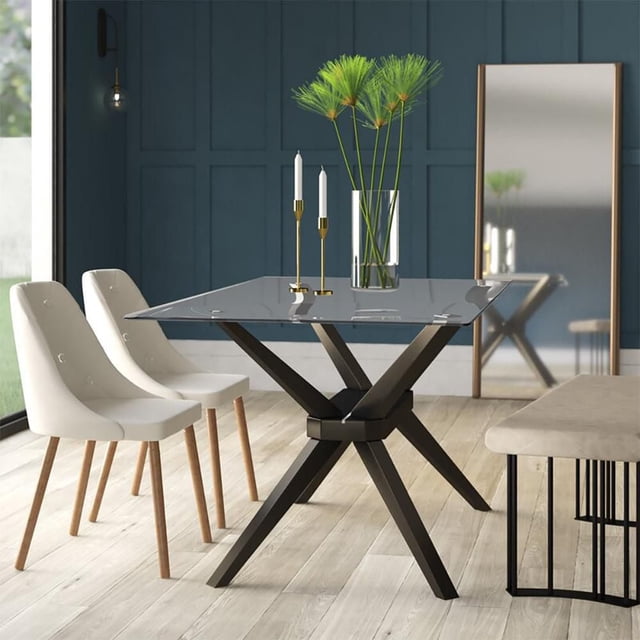 Home Gear Dining Table with a 63-inch by 35.4-inch clear tempered glass rectangular top on a dark walnut solid wood trestle base with flared legs, designed to seat six. Shown in a dining room with light hardwood floors, two white upholstered chairs with wooden legs, a beige bench with black metal frame, a full-length mirror, and decorative items including a glass vase with green papyrus stems and two gold candlesticks with white taper candles.