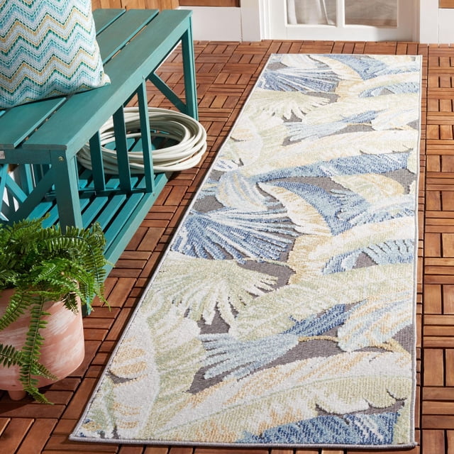 SAFAVIEH Sarasota Olivia Tapis d'Aire Floral Intérieur/extérieur sur une Terrasse en Bois, Présentant une Forme Rectangulaire avec des Motifs Floraux Bleu, beige et Vert Atténués. Placé à Côté d'Un Banc en Bois Sarcelle avec un Coussin à Motifs et un Tuyau d'Arrosage Blanc Enroulé, Près d'Une Fougère en Pot. Ce Tapis d'Aire Extérieur Résistant aux Intempéries Est Idéal pour Rehausser le patio Ou les Espaces Intérieurs.