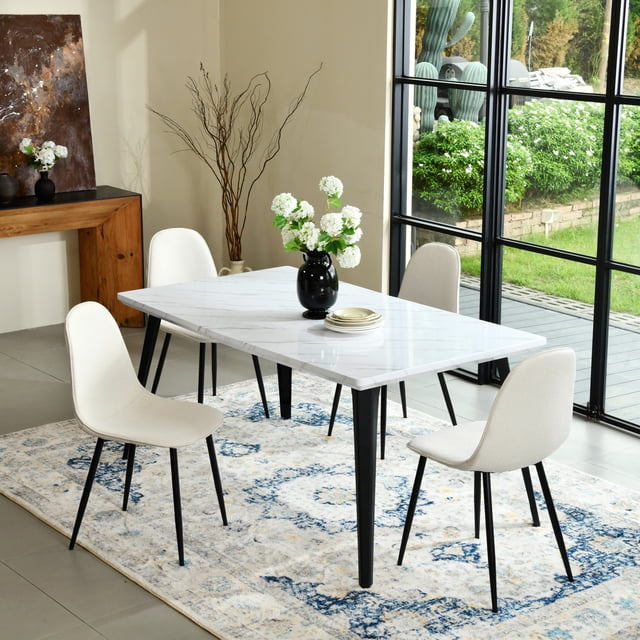 Homy Casa 63 inch modern dining set with a rectangular faux marble tabletop and black metal legs, paired with four beige fabric upholstered chairs with supportive backs and black tapered legs, set on a blue and beige patterned rug near large black-framed windows overlooking a garden, ideal for kitchen or dining room spaces.