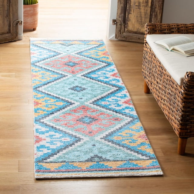 Safavieh Saffron Franklin Tapis Géométrique pour Aire sur un Plancher de Bois Franc Clair, Présentant un Tissage de Coton durable avec des Motifs Géométriques Colorés en Losanges en Bleu pastel, Corail, Jaune et Gris, Placé à Côté d'Un Banc en Osier avec un Coussin Blanc et un Livre Ouvert, Idéal comme Tapis d'Accent pour la Déco de la Maison et Souvent Utilisé pour Égayer les Espaces Étroits.