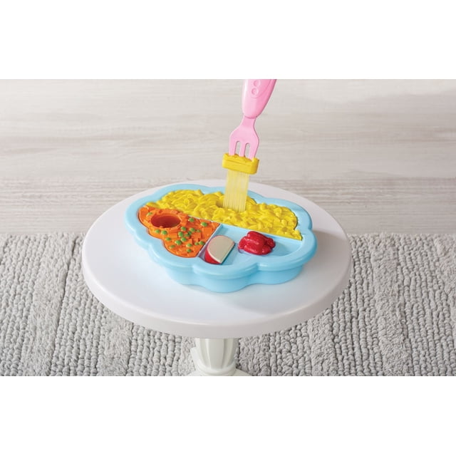 My Sweet Baby Magic Baby Food Play Set with a blue divided food tray containing yellow mac & cheese, orange vegetables with green peas, a red sauce portion, and a pink fork lifting mac & cheese, set on a white round table over a grey textured rug.