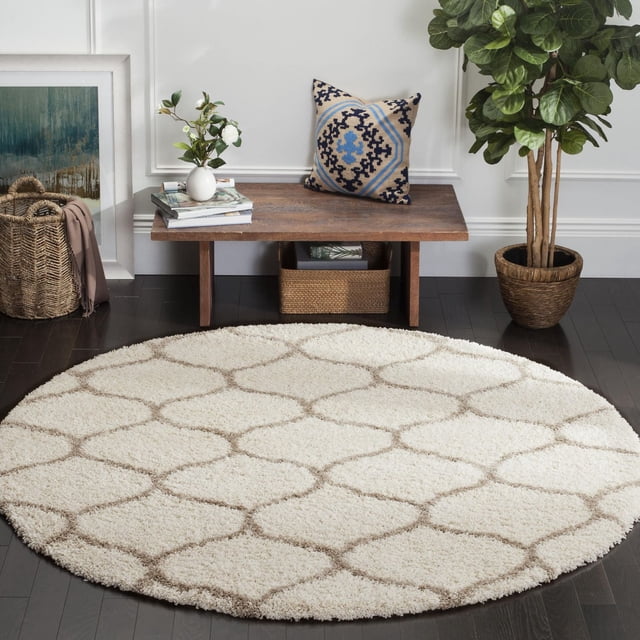 Safavieh Hudson Tapis Shag Géométrique Arline, Rond avec une Épaisse pile Shag Ivoire et Motif de Carreaux Géométriques Brun Clair, Posé sur un Plancher de Bois Franc Foncé dans un Cadre Contemporain avec un Banc en Bois, un Coussin Décoratif, une Plante en Pot et un Panier Tressé.