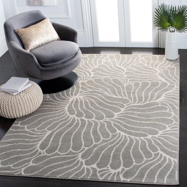 Safavieh Pyramid Tapis Floral Katherina avec Fils Synthétiques à Poils Mi-Coupés en Gris avec un Motif Floral Blanc, Exposé sur un Plancher de Bois Franc Foncé à Côté d'Une Chaise Pivotante Grise avec un Coussin Décoratif beige, un pouf Tricoté avec des Livres et un vase Blanc Tenant des Feuilles de Palmier Vertes Près des Fenêtres Lumineuses, Idéal pour Améliorer la Chaleur et le style dans la Déco de la Maison.