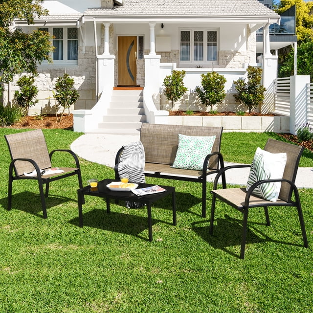 Gymax Ensemble de Conversation pour Patio 4 Pcs en Brun, Incluant un Causeuse, Deux Chaises Ergonomiques et une table Basse avec un Cadre en Acier Noir et un Tissu Imperméable. l'Ensemble Est Disposé sur une Pelouse Verte devant une Maison Blanche, Accessoirisé avec des Coussins à Motifs et de la Vaisselle sur la table Basse.