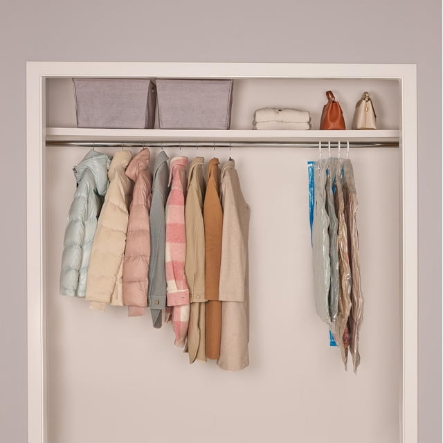 MAINSTAYS Hanging Vacuum Bags hanging in a closet on a metal rod with coats and jackets. The vacuum bags compress bulky garments on the right side, maximizing storage space and protecting clothes from dust and moisture. Above, gray fabric bins, folded linens, and handbags are neatly arranged on a shelf, creating an organized and space-efficient storage solution.
