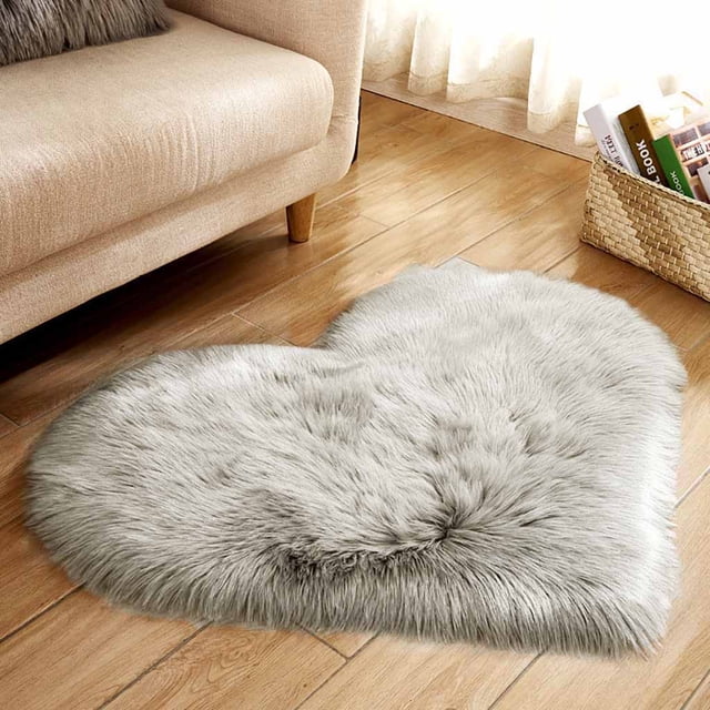 Agiferg Wool Imitation Sheepskin Rugs Faux Fur Non Slip Bedroom Shaggy Carpet Mats in grey, shown in a heart-shaped design on a wooden floor. The faux fur rug features a soft, shaggy texture made of durable polyester, offering underfoot comfort. Positioned near a beige sofa and a woven basket, it complements the cozy, modern decor.