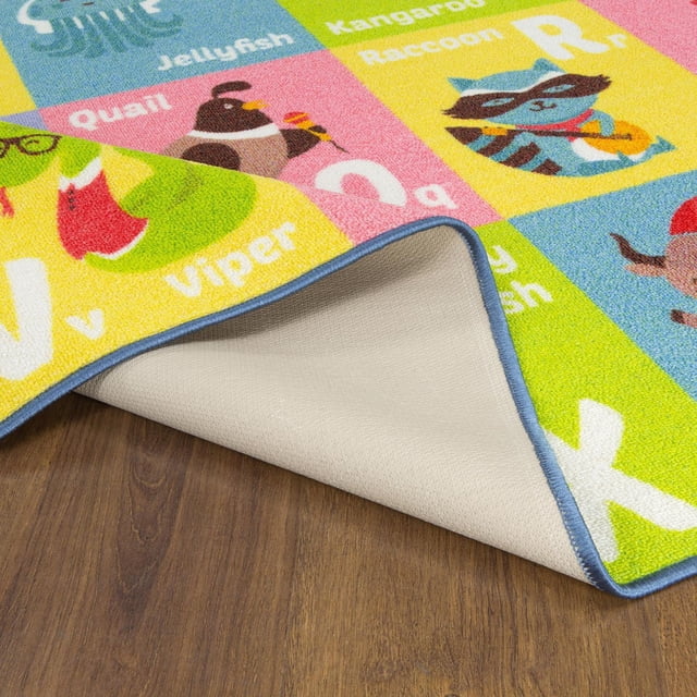 KC Cubs Playtime Collection ABC Alphabet Animal Educational Learning & Game Area Rug Carpet for Kids and Children Bedrooms and Playroom showing a close-up of the colorful rug corner flipped to reveal a beige non-slip backing, featuring illustrated animals like raccoon, quail, and viper with their corresponding letters on a wood floor.