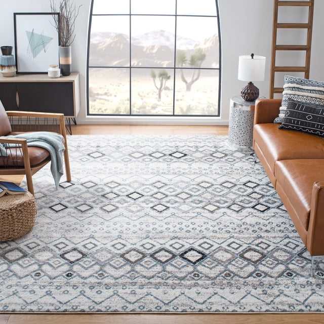 SAFAVIEH Amsterdam Gladwin Geometric Area Rug with a light earth-tone pile and geometric diamond pattern in gray, blue, and beige hues, placed on a hardwood floor between a brown leather sofa and a wooden armchair with a blue throw. The durable accent rug complements rustic-chic home décor and is ideal for living rooms with natural light and warm tones.