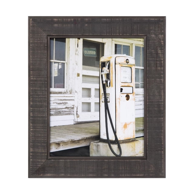 hometrends Healdton Black Picture Frame showing a vintage white gas pump with rust spots on a concrete base outside a weathered wooden building with peeling white paint and a closed sign on the door, enclosed in a textured black frame with inner and outer curved bevels.