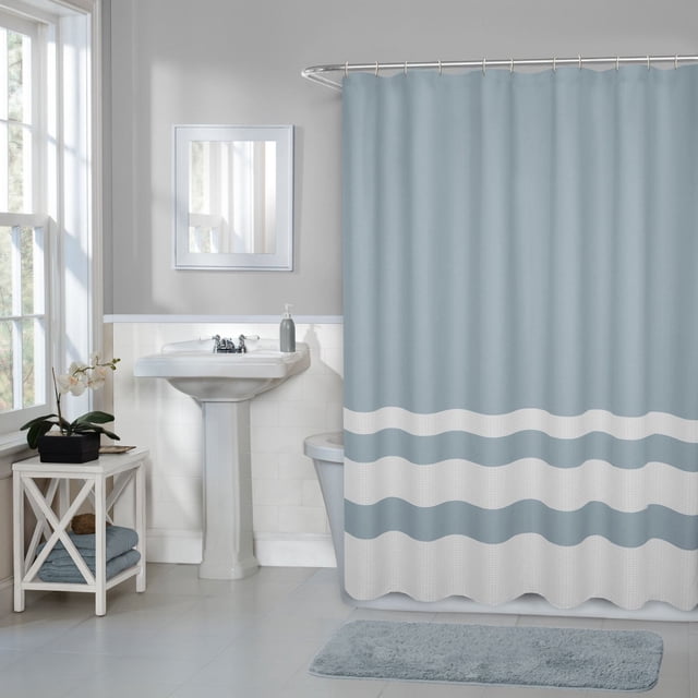 Hometrends Textured Waffle Stripe Fabric Shower Curtain in light blue with two-toned white waffle stripe design, measuring 70 by 72 inches, hanging on a curved shower rod in a bathroom with white pedestal sink, mirror, and matching light blue bath mat, suitable for standard tubs and showers.