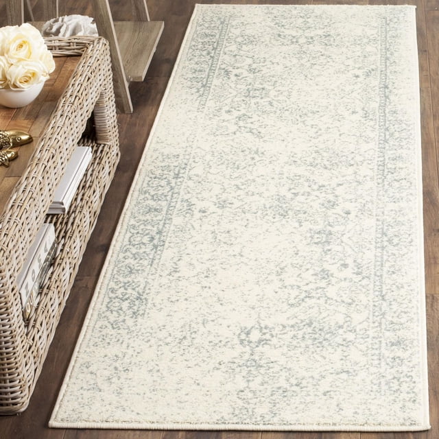 SAFAVIEH Adirondack Wyatt Tapis Traditionnel pour Aire avec un Fond Crème Pâle et des Motifs Traditionnels Gris Subtil Surteints, Tissé Mécaniquement à Partir de Fils de Polypropylène Durables, Montré sur un Plancher de Bois Franc à Côté d'Une Étagère en Osier avec des Articles Décoratifs, Idéal pour les Milieux Rustiques Ou Urbains et Convient aux Pièces à Fort Passage.