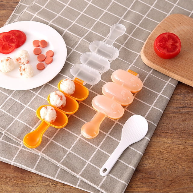 HBBKVI Kitchen Essentials Wobble Le Rice Ball Molds, a set of three small spherical molds in orange and translucent colors, ideal for crafting evenly shaped rice balls. Featured on a checkered tablecloth with a white rice paddle, sliced tomatoes, and prepared rice balls, this kitchen gadget is perfect for specialty kitchen tasks.