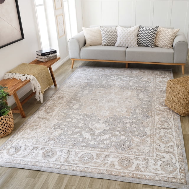 Rug Branch Cadence Vintage Indoor Area Rug in beige grey with an oriental floral pattern, measuring 6'3" x 9'6", displayed in a bright living room with a light grey sofa featuring chevron and textured cushions, a wooden bench with a mustard throw, and a woven basket on light wood flooring, ideal for living room, bedroom, dining room, or kitchen.
