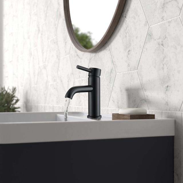 Ancona Valencia Series Single Lever Bathroom Faucet in Matte Black installed on a modern bathroom sink. The faucet features a pivot-action single lever for precise temperature and water flow control, constructed from lead-free solid brass with a premium ceramic disc cartridge for drip-free operation. The matte black finish complements the hexagonal tile backsplash and round mirror in the bathroom setting. Designed for single-hole installation and cUPC certified for quality assurance.