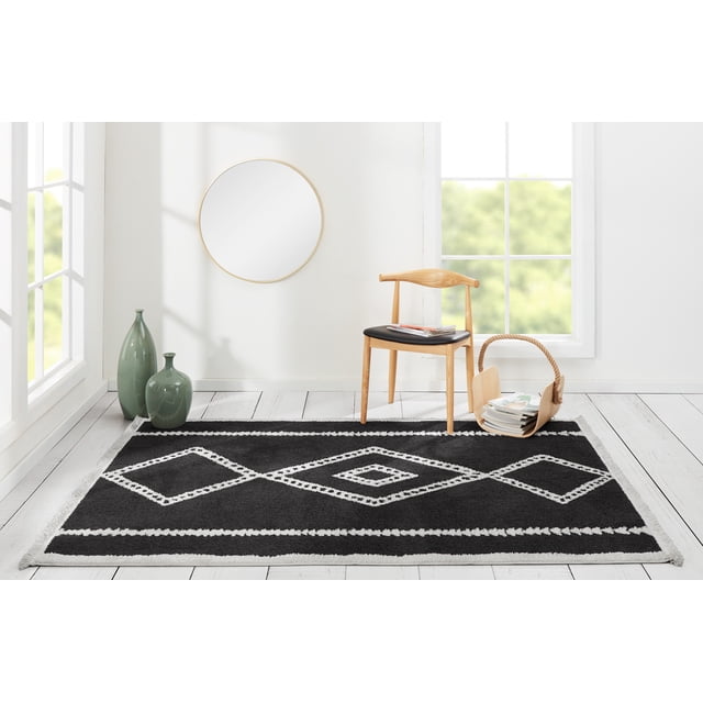 ECARPET Zelda contemporary black area rug featuring white geometric diamond patterns displayed in a bright living space with wooden chair, basket of magazines, and decorative green vases