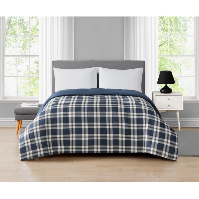Mainstays Plaid Navy Reversible Comforter Twin on a bed with a gray upholstered headboard, featuring a navy and white plaid microfiber polyester front and solid navy reverse, in a bright room with white curtains, two white pillows, a gray bench with books, and a white nightstand with a black lamp, machine washable and suitable for adult or kids rooms.