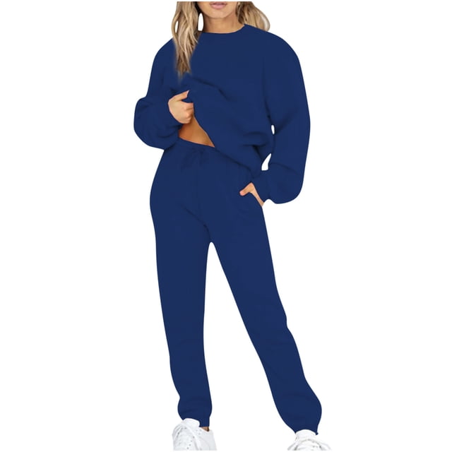 Cameland Jogging Suits For Womens 2 Piece Long Sleeve Sweat Suit Solid Color Winter Fleece Tracksuits. The image shows a woman wearing a solid navy blue two-piece tracksuit, featuring a long-sleeve sweatshirt and matching jogger pants with an elastic waistband. The outfit has a loose fit and is made of soft polyester fleece, suitable for casual wear, workouts, or lounging during winter and spring. The model pairs the tracksuit with white sneakers.