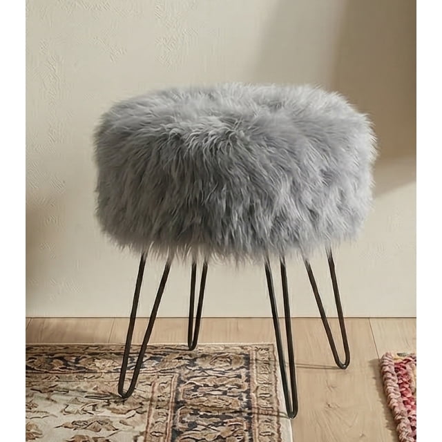 Ottoman Rond Pixie, Pouf, Repose-Pieds, Tabouret Repose-Pieds avec Siège Rond en Fausse Fourrure Gris et Pattes Épingle en Métal Noir. l'Ottoman Mesure 16 Pouces de Hauteur de Siège et 14,5 Pouces de Diamètre de Siège, Offrant une construction Robuste avec une Capacité de Poids de 300 Lb. Idéal pour Salons, Chambres, Couloirs Ou Salles de Bain, Il Ajoute une Touche Luxueuse Tout en Offrant un Assise Fonctionnelle. Présenté dans un Décor Intérieur Douillet avec un Tapis à Motifs et un Plancher en Bois.