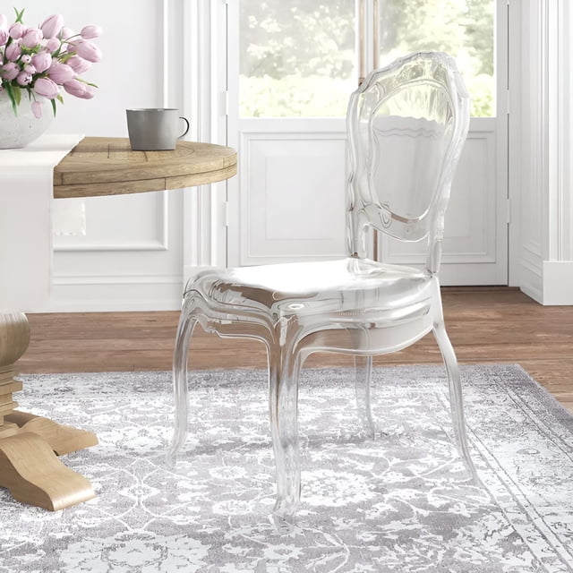 Heavenly Collection Clear Plastic Armless Chair made of transparent polycarbonate with a curved backrest and four legs, set on a grey and white patterned rug beside a wooden dining table with a grey mug and pink flowers in a bright room with white walls and large windows, suitable for modern living spaces.