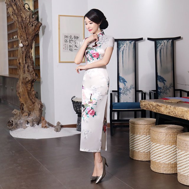 Robe Qipao Longue pour Femmes Multicolore Rétro Classique Style Chinois Imprimée Qipao Grande Taille Coupe Ajustée. la Robe Présente un design Chinois Traditionnel avec un Col Montant, des Manches Courtes et une silhouette Ajustée. Elle Est Ornée d'Un Imprimé floral vibrant sur un Fond Léger, s'Étendant jusqu'à la Cheville avec des Fentes Latérales pour une Facilité de Mouvement. Fabriquée en Tissu Léger et Respirant, Elle Convient à des occasions comme les Mariages, les Réunions de Famille Ou le Port Quotidien. le Cadre Montre la Robe Stylisée avec des Talons Métalliques dans un Intérieur Moderne avec des Éléments de Déco Chinois Tradition