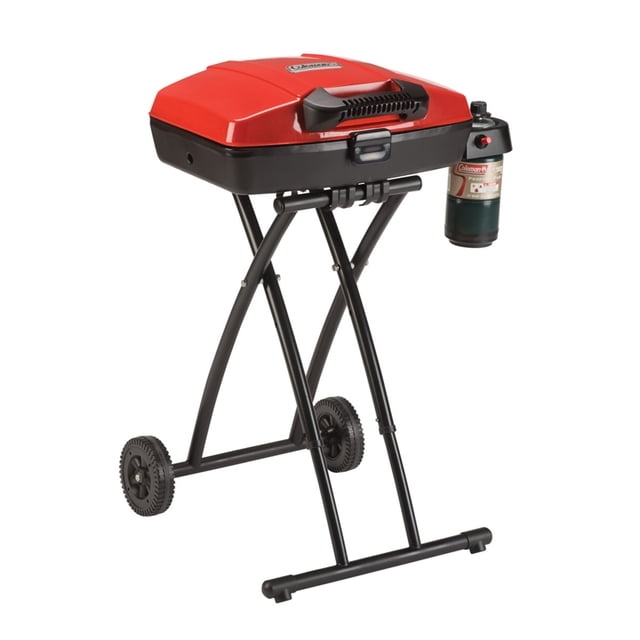 Coleman RoadTrip Sportster Propane Gas Grill with red lid and black base on a collapsible wheeled stand, featuring a propane cylinder on the right, porcelain-coated steel grate, removable grease tray, and 11,000 BTUs cooking power, suitable for tailgates and camping trips.
