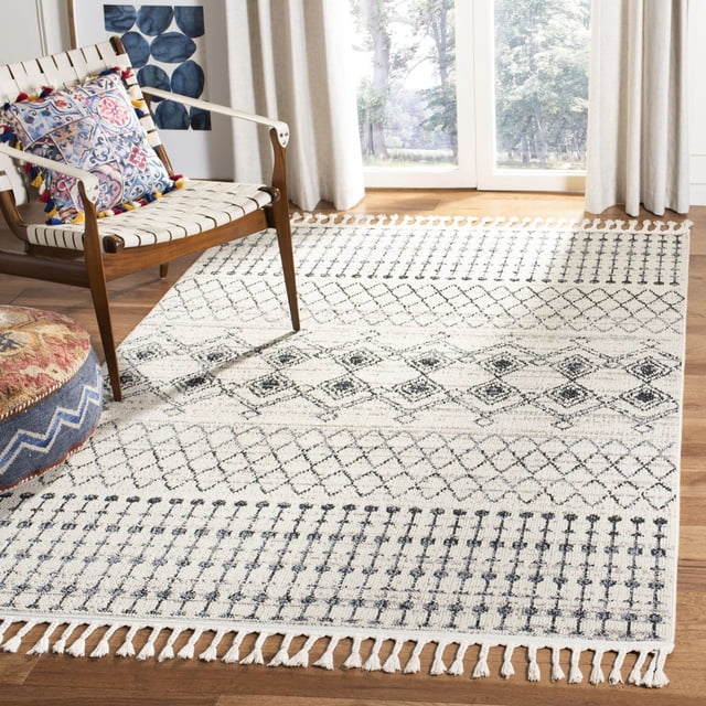 Safavieh Marrakesh Tapis d'Été Style Sud-Ouest à Franges Crème avec Motifs Géométriques Tribaux Noirs et Bords à Franges, Posé sur Plancher de Bois Franc Près d'Une Chaise à Lanières Tressées en Bois avec un Coussin à Pompons Colorés, dans une Pièce Ensoleillée avec de Grandes Fenêtres et des Rideaux Légers, Souvent Utilisé pour Ajouter une Touche Bohème-Chic aux Espaces de Vie.