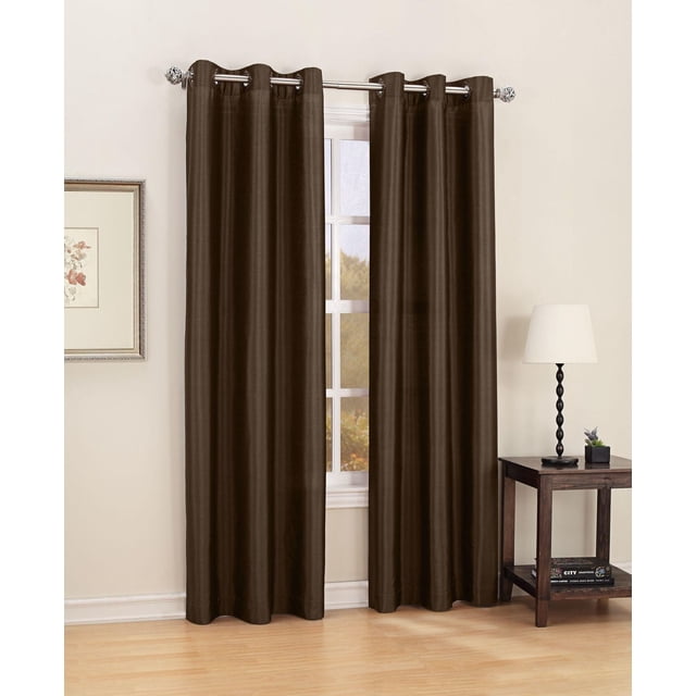 SASHA FAUX SILK GROMMET CURTAIN PANEL in mocha polyester fabric with silver grommets, hanging on a curtain rod over a window in a neutral room with light wood flooring, a framed floral print on the left wall, and a dark wood side table with a black twisted lamp and small plant on the right, designed to filter light and machine washable on gentle cycle, also suitable for adding a warm, elegant touch to living spaces.