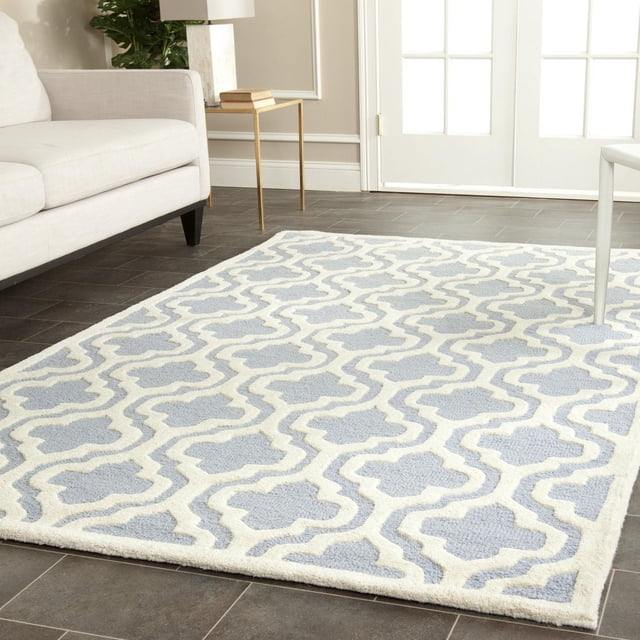 Safavieh Cambridge Kirsten Tapis Géométrique pour Salon avec Revêtement de Sol en Carreaux Foncé, avec Laine Tuftée à la Main avec Boucle Texturée Haut/bas et Poil Coupé en Motif Géométrique Bleu Pâle et Crème, Placé Près d'Un sofa Blanc et d'Une table d'Appoint Dorée avec des Livres.