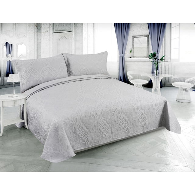 Marina Decoration Solid Embossed Pinsonic Coverlet Bedspread Bedding Ultra Soft Summer Quilt Set with Shams in silver color on a bed in a bright room with white walls and blue curtains. The quilt features a solid silver tone with an embossed floral pattern in breathable brushed microfiber fabric. The set includes matching pillow shams and is lightweight, reversible, wrinkle-free, and machine washable. Ideal for all-season comfort and also suitable as a lightweight blanket or bedsheet alternative.