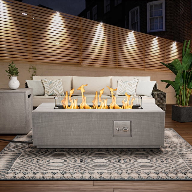 Evita Table de Foyer au Propane de 42 Pieds' 50 000 BTU avec Flamme Réglable Exposée dans un Décor de patio Extérieur. la Table Rectangulaire de Foyer Présente un design Moderne avec un Cadre en Acier, des Panneaux Latéraux en Osier et un Brûleur central en Acier Inoxydable Entouré d'Un Verre Pare-Vent Trempé. la Table Est Présentée avec une Flamme Vibrante et Comprend un Verre Pare-Vent Bleu. Elle Sert Aussi de Table à Manger Ou à Café Lorsque le Couvercle Est en place. des Accessoires comme une Housse de Pluie et un Couvercle de Foyer Amovible Sont Inclus.