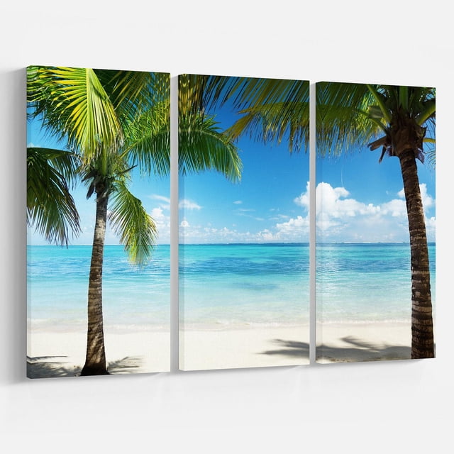 Designart Palm Trees and Sea Canvas Wall Art with three gallery-wrapped cotton canvas panels depicting two green palm trees on a white sandy beach beside turquoise sea under a blue sky with clouds, printed with fade-resistant ink and ready to hang for coastal home décor.