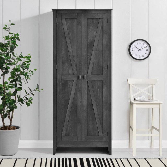 Farmington 31.5" Wide Storage Cabinet in rustic grey with barn-style X panel doors and tapered feet, front-facing against a white paneled wall, flanked by a potted green plant and a white wooden chair under a round wall clock, suitable for storing office supplies, linens, or seasonal items.