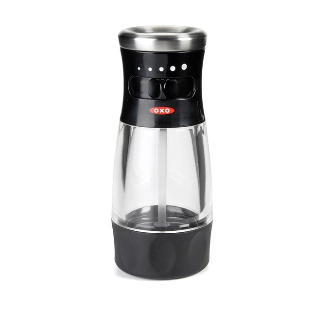 OXO Softworks Salt Grinder with clear acrylic body, black non-slip grip base, stainless steel top, and adjustable grind selector with five settings from fine to coarse. Includes a manual ceramic grinder, airtight lid, and red OXO logo on the black upper section.