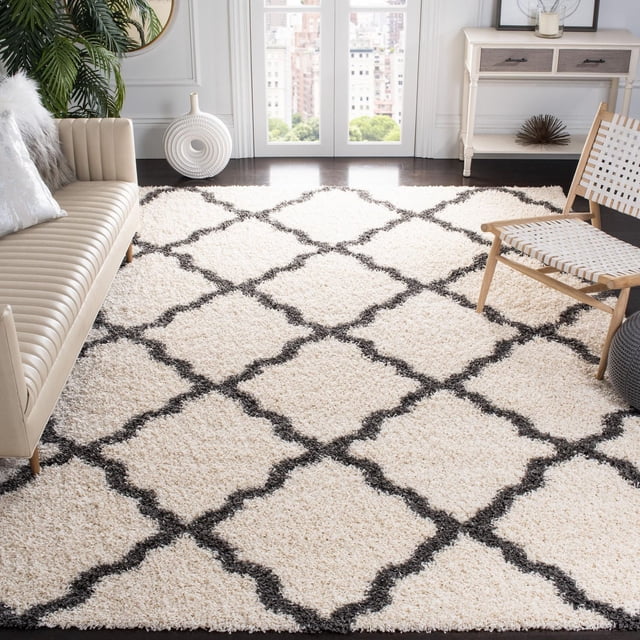 Safavieh Dallas Tapis Shag Géométrique Logan avec Poils Shag Ivoire Moelleux et Motif de Carreaux Marocains Sombres, Tissé Mécaniquement en Polypropylène Facile d'Entretien. Exposé dans un Salon Lumineux entre un sofa en Cuir beige et une Chaise en Bois avec Siège Blanc Tressé, Près de Grandes Fenêtres Surplombant un Paysage Urbain. Idéal pour Ajouter une texture Douce et un style Géométrique aux Intérieurs de la Maison.